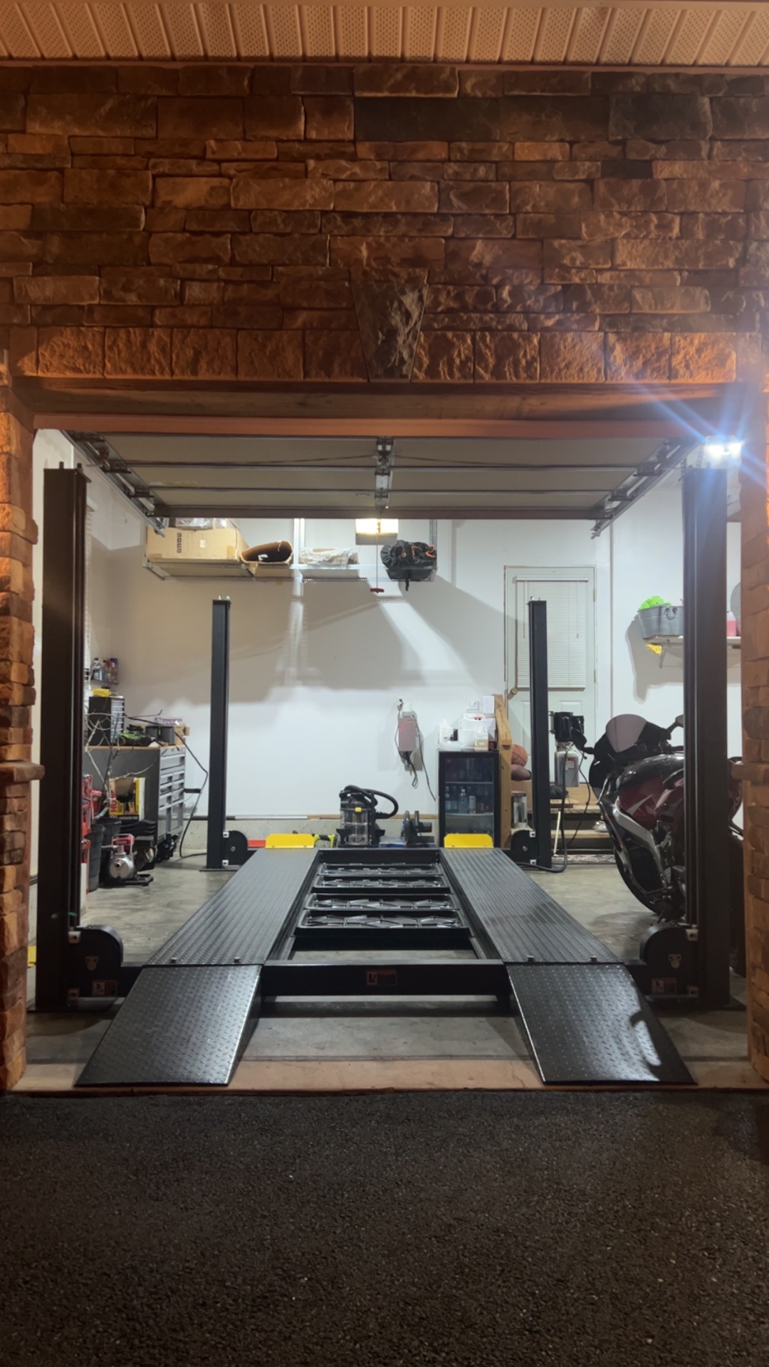 Four-post lift installed in a stone-front residential garage at night
