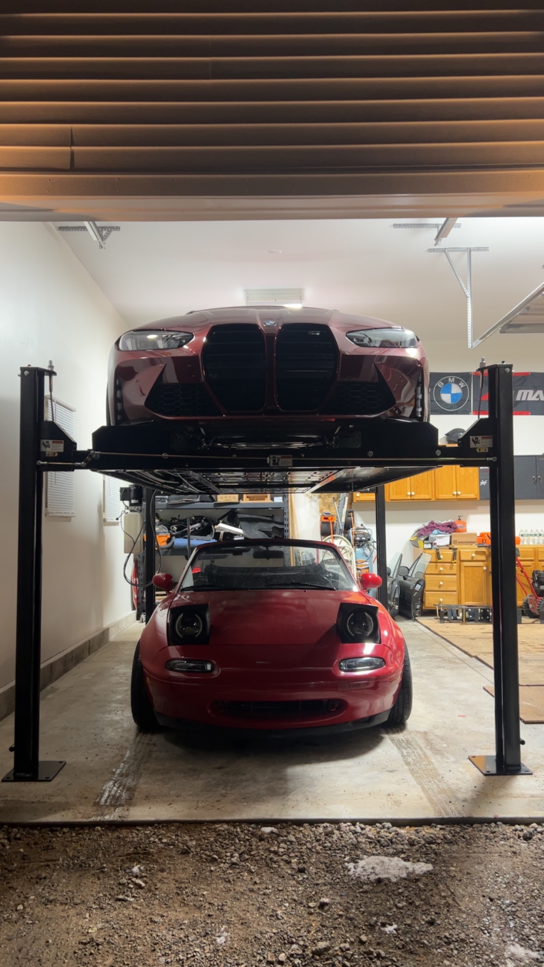 Four-post lift storing a BMW M4 above a Mazda Miata